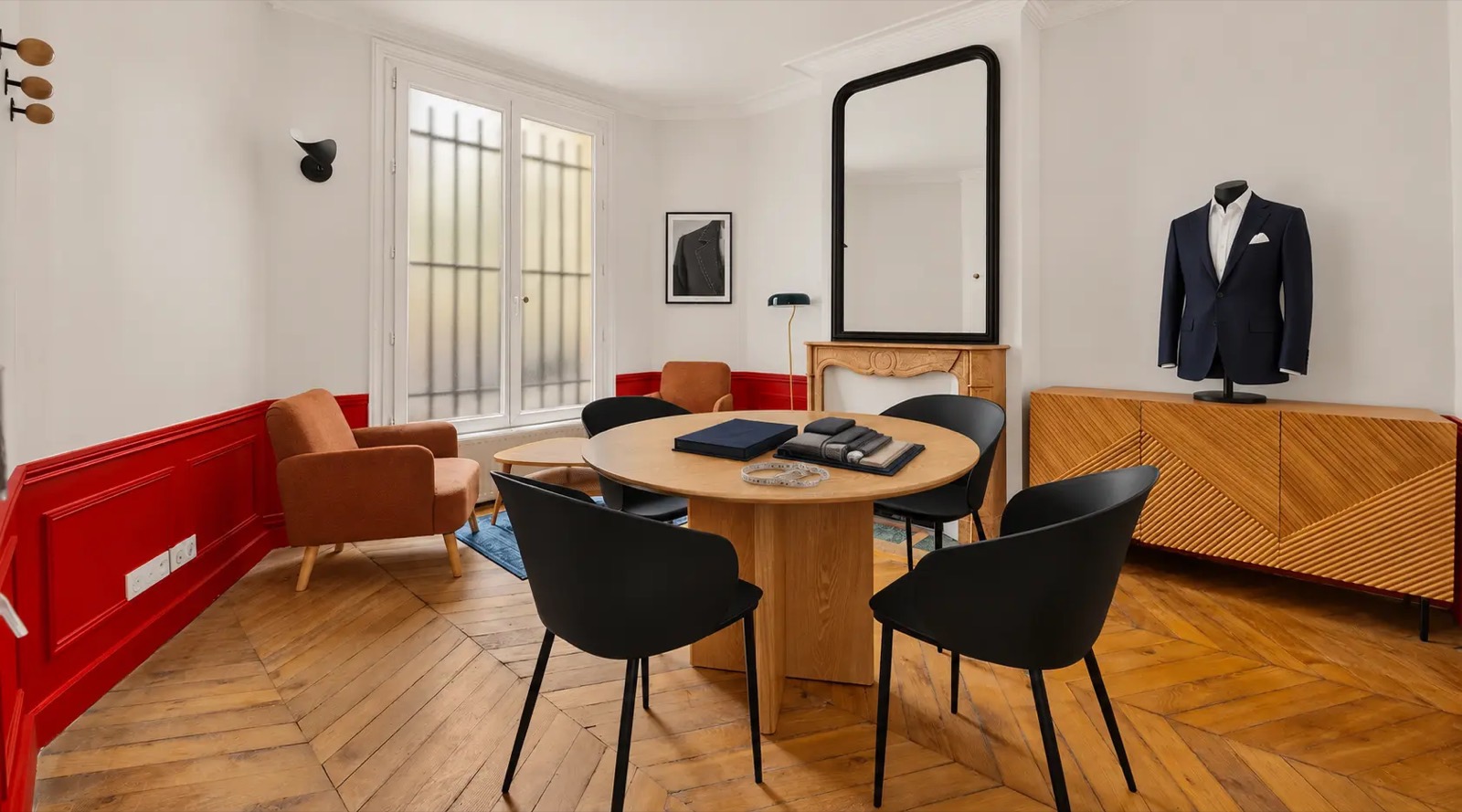 Le salon Madeleine : table ronde de sélection des tissus, soubassements rouges et veste sur mannequin